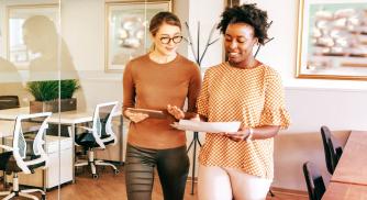 Two female employees walking and having a conversation in a conference room