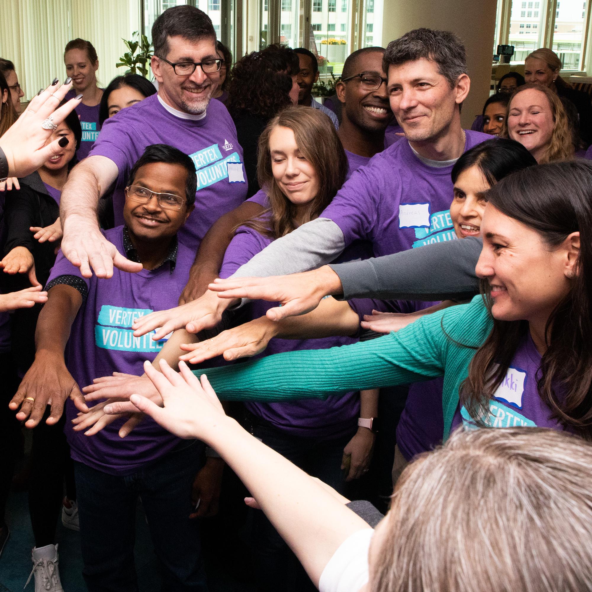 An image of a group of Vertex employees all putting their hands together in a circle