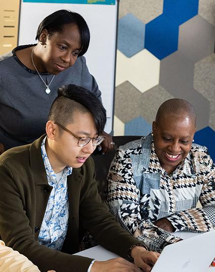 A group of 4 Vertex employees viewing content on a laptop