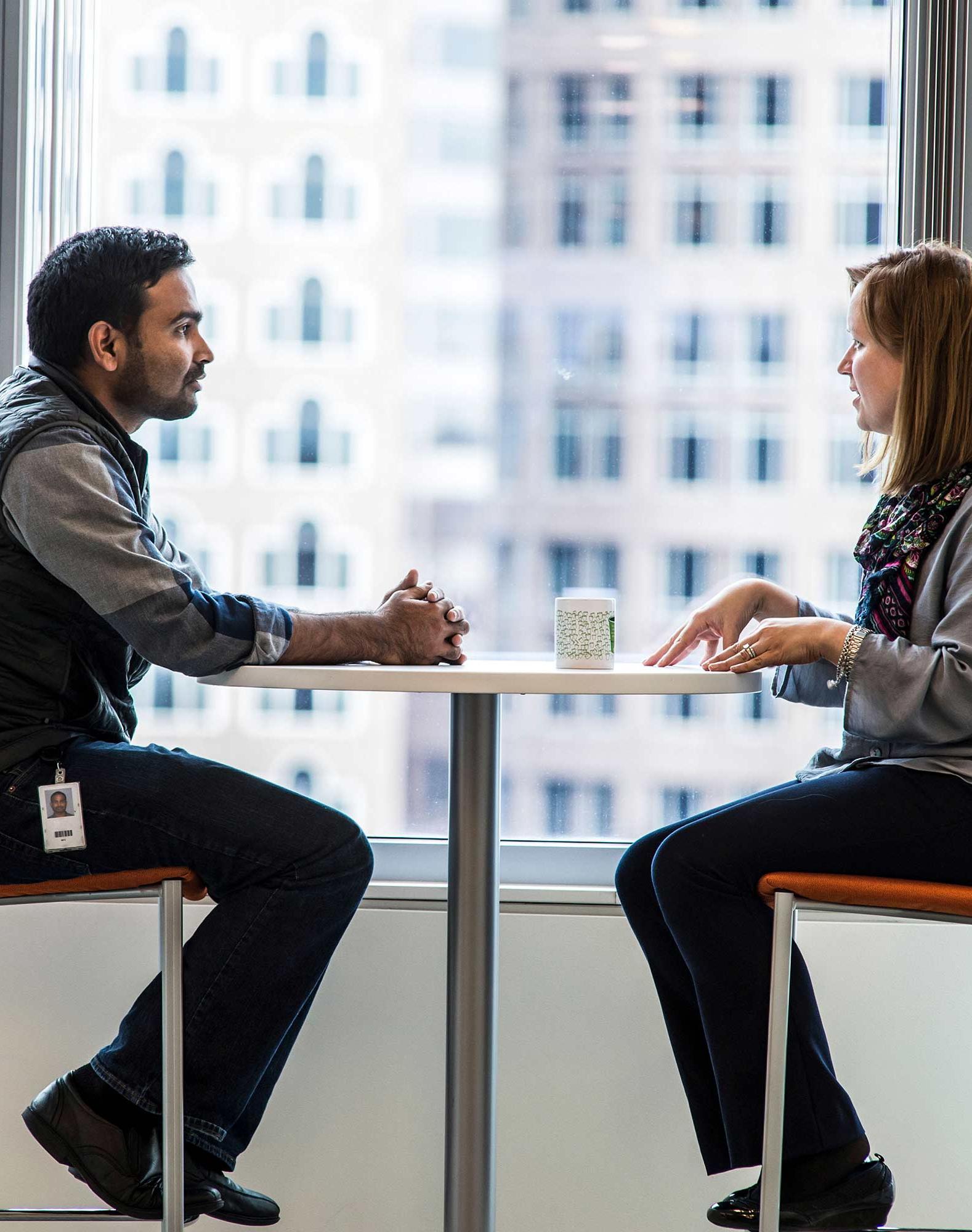 Two Vertex employees sitting by a window having a discussion