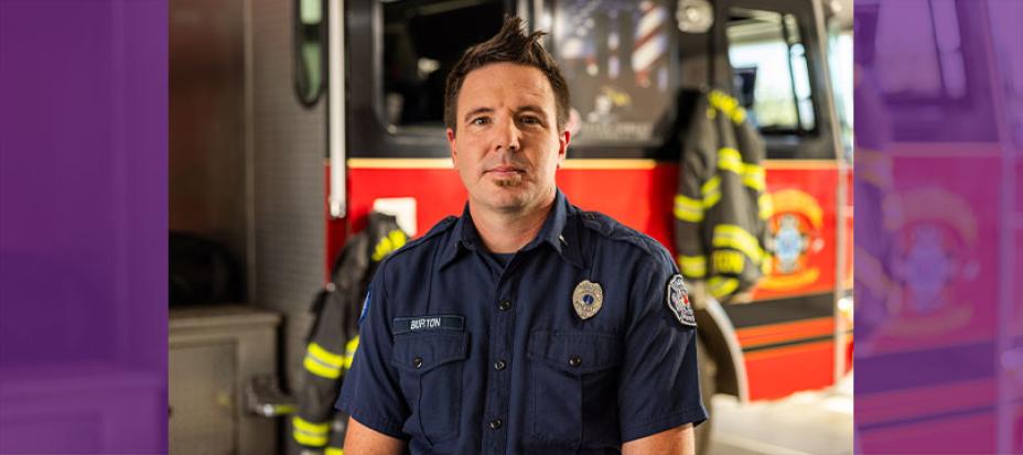 An image of Cody Burton standing in front of a firetruck wearing his firefighter uniform.