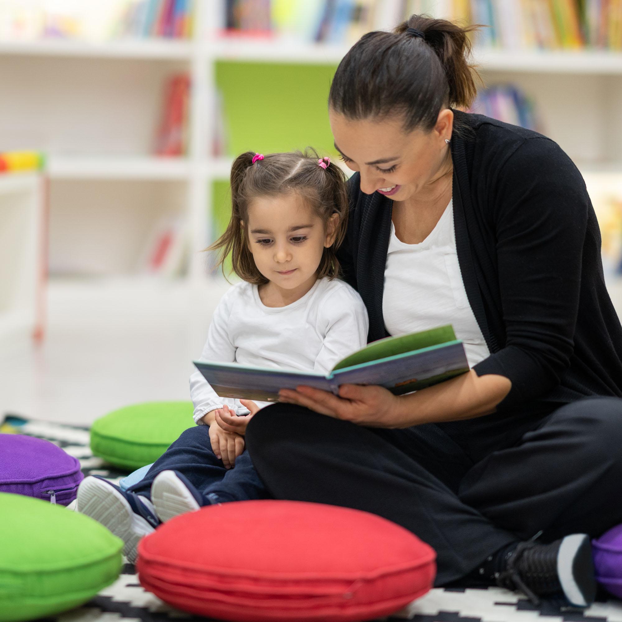 A mother and daughter reading a book together while sitting on the floor