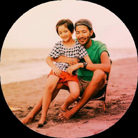 A man and daughter sitting on the beach at sunset