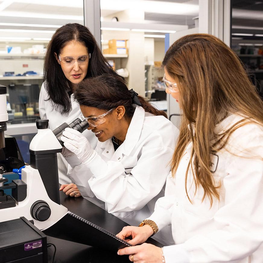 An image of 3 Vertex scientists in the lab and one of them is using a microscope