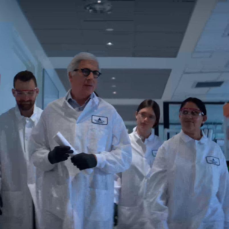 An image of 4 Vertex scientists wearing lab coats walking down a hallway