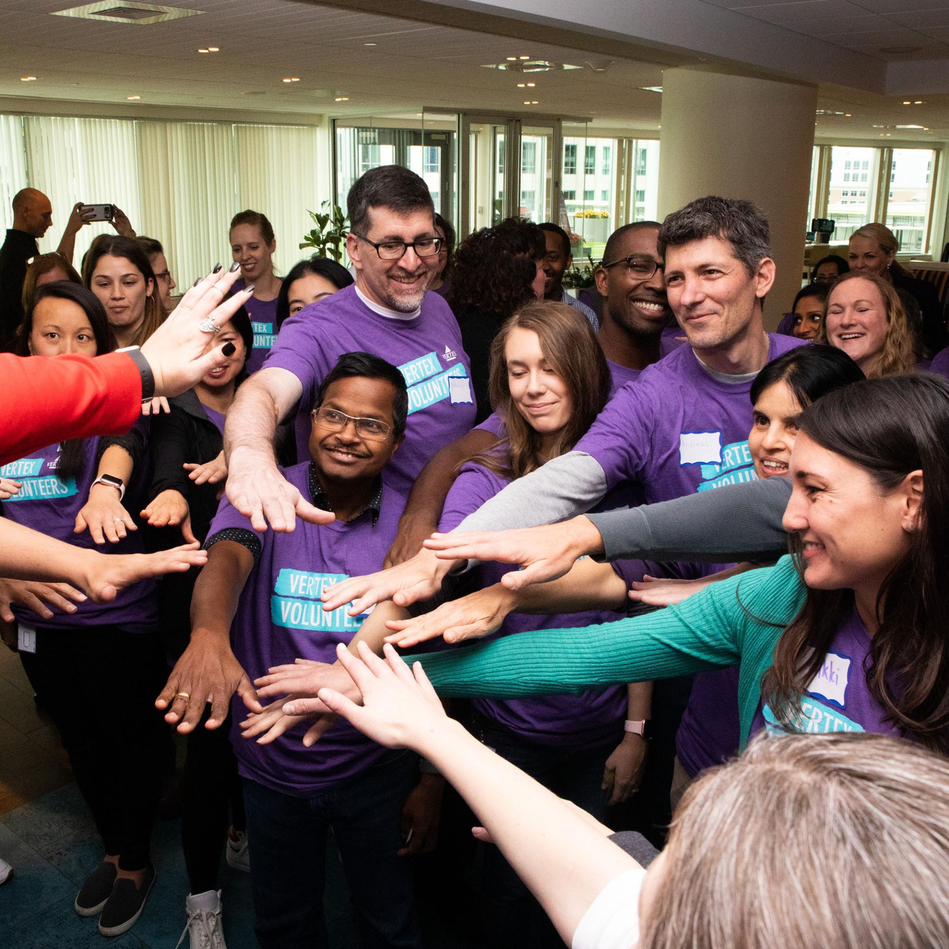 An image of a group of Vertex employees all putting their hands together in a circle